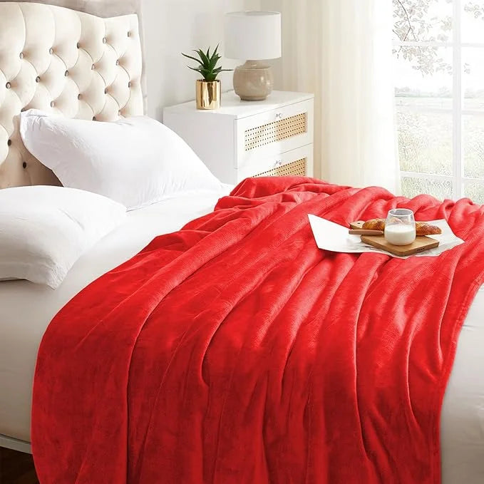 Red blanket draped over a bed with white pillows and a nightstand in the background.