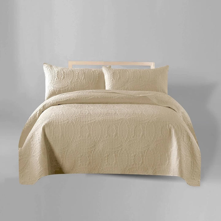 Beige quilt set with pillows on a bed against a gray background