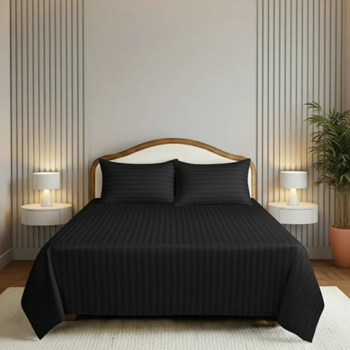 Black bedspread set on a bed in a bedroom with two lamps and a plant.