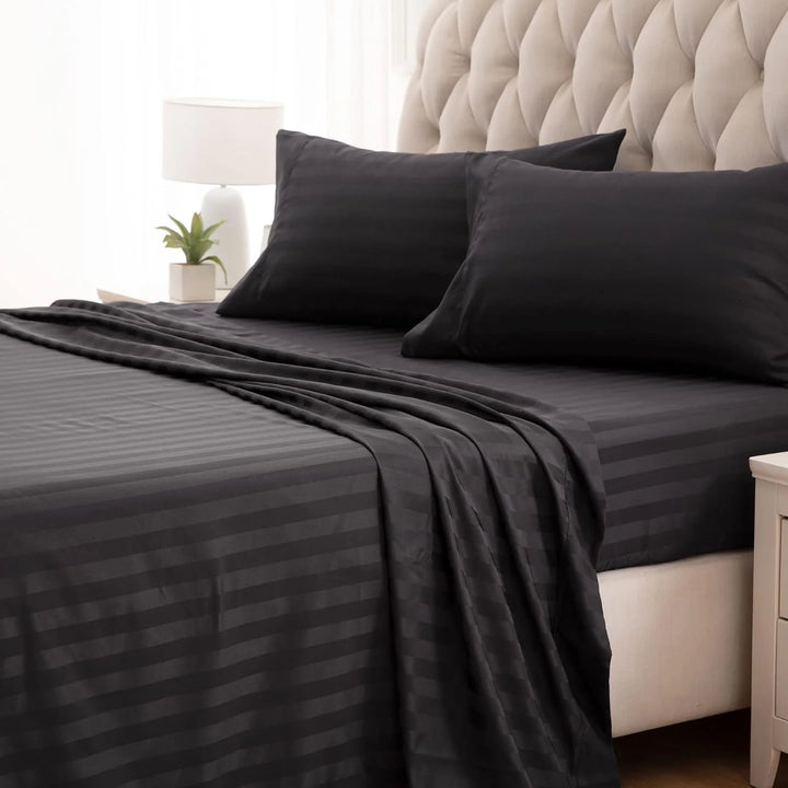 Black bed sheets and pillows on a bed with a beige headboard.
