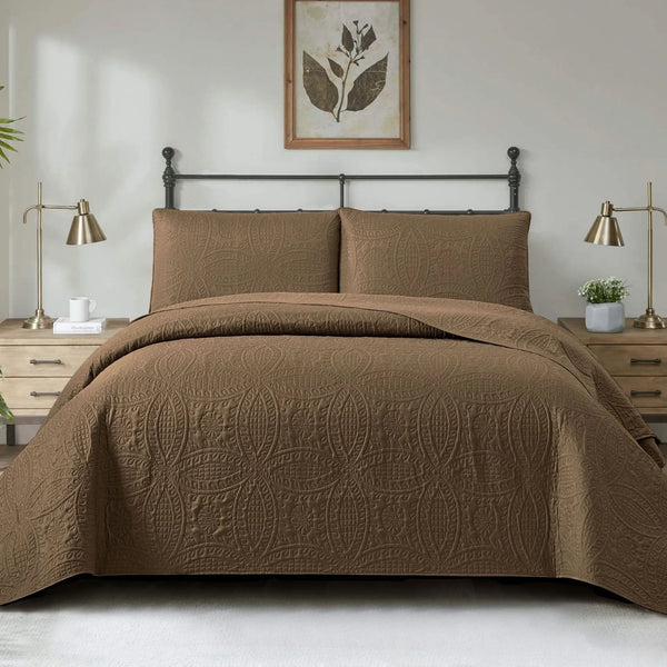 Brown quilted coverlet set on a bed in a bedroom with two lamps and a framed picture on the wall.
