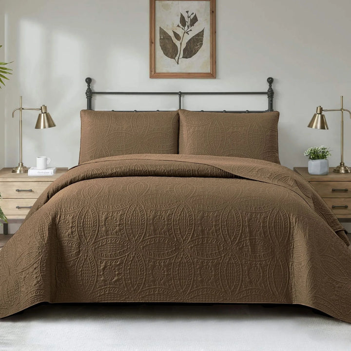 Brown quilted coverlet set on a bed in a bedroom with two lamps and a framed picture on the wall.