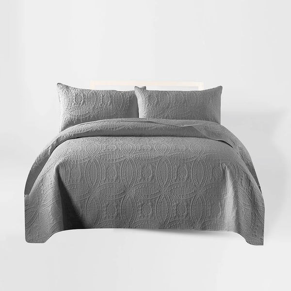 Gray quilt set with matching pillows on a bed against a white background