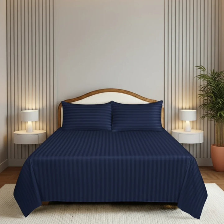 Navy blue bedspread set on a bed in a bedroom with striped walls and lamps.