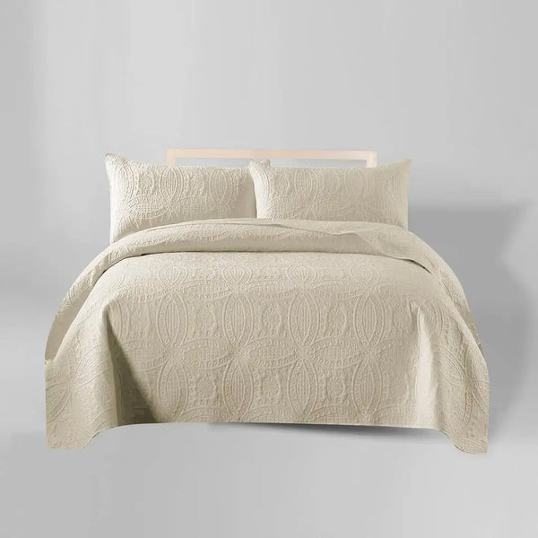 Beige quilt set with pillows on a bed against a gray background