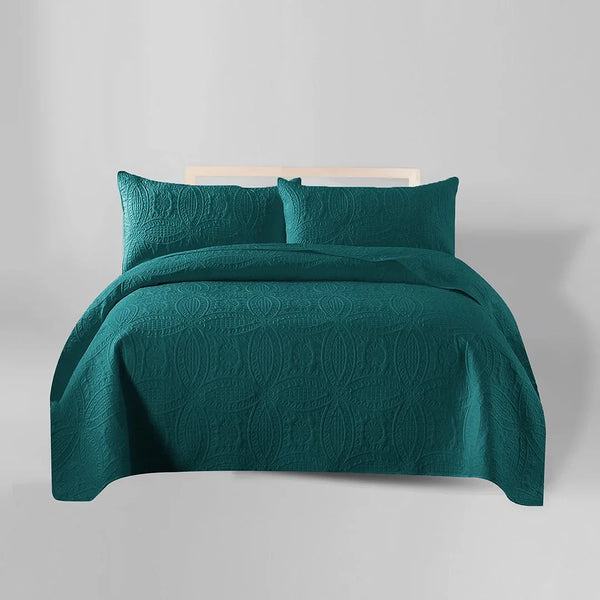 Teal quilt and pillow set on a bed against a gray background